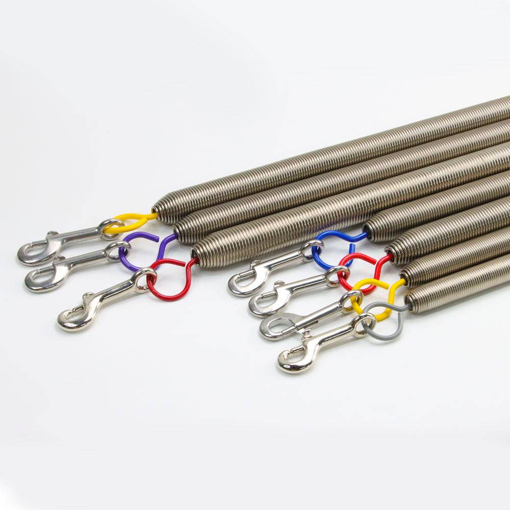 Close-up of Pilates Trapeze Springs for Cadillac and Wall Tower showing rust-proof steel coils and red, yellow, and blue color-coded connectors.